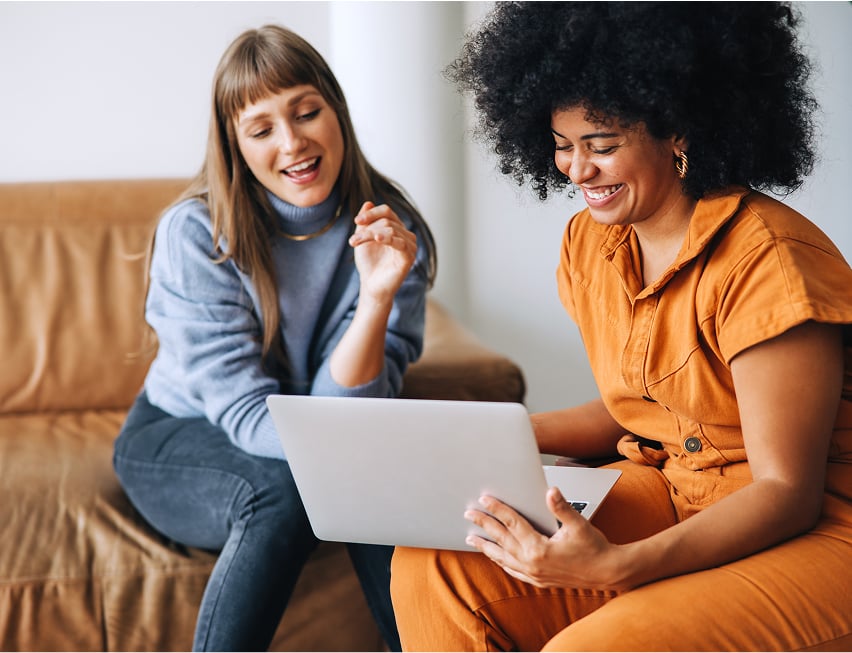 Two people looking at a laptop together while sitting on a sofa