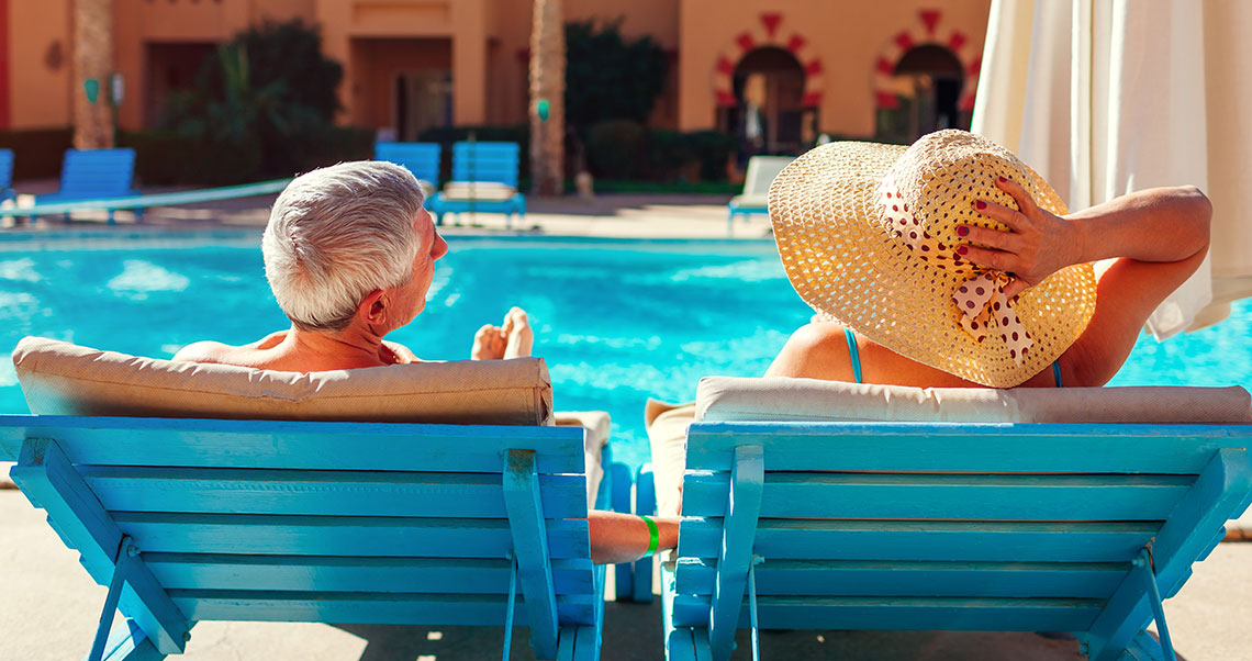 Elderly couple sunbathing in front of a pool